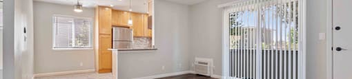 Milpitas, CA Apartments - Spring Valley - Open-Floor Living Room With High Ceiling, Wood-Style Flooring, Modern Light Fixtures, AC Unit, Glass Sliding Doors With Blinds, And Access To Kitchen
