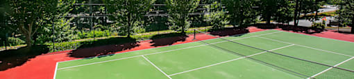 A tennis court with red and green surface surrounded by trees.