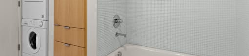A white tiled bathroom with a wooden cabinet and a white bathtub.
