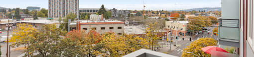 A balcony overlooks a city street with buildings and trees.