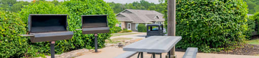 two grills and a picnic table in a park with benches
