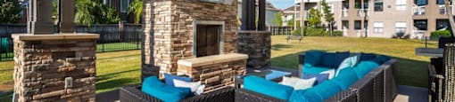 1 BR Apartments in League City, TX - Anchor at South Shore - Outdoor Lounge with Cozy Seating, a TV, a Fireplace, and a Ceiling Fan
