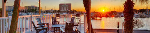 a deck with chairs and palm trees overlooking the water at sunset