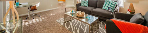 League City, TX Apartments - Anchor at South Shore - Furnished Living Room with Carpet Flooring, Large Windows with Blinds, Stylish Decor, and a Dining Area Near the Kitchen