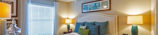 2 BR Apartments in League City, TX - Anchor at South Shore - Bedroom with Carpet Flooring, a Bed, a Ceiling Fan, and a Large Window with Curtains and Blinds