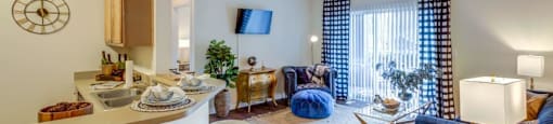 Two-Bedroom Apartments in San Antonio, TX - Club at Stone Oak - Living Room with Wood-Style Flooring, a Couch, Chair, Coffee Table, End Tables with Lamps, TV, and Sliding Glass Door