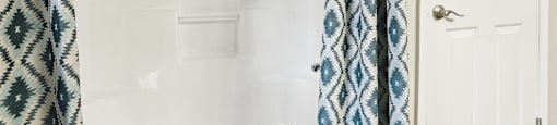 A white door is next to a bathtub with a blue and white shower curtain.