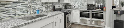 A modern kitchen with white cabinets and a stone backsplash.