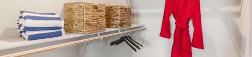 A red robe is hanging on a rack in a white closet.
