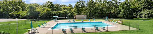 a swimming pool in the middle of a grass field with chairs around it