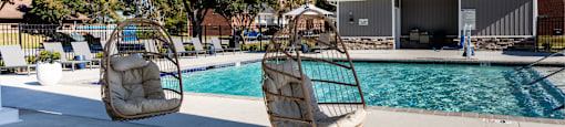 Two hanging chairs over a pool with a house in the background.