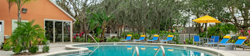 a swimming pool with blue and yellow chaise lounge chairs and trees in the background