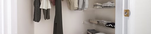 A white closet with clothes hanging and drawers on the floor.