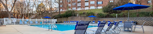 A pool with chairs and umbrellas is surrounded by a brick building at Amelia Village apartments in Clayton, NC.