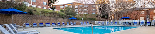 A pool surrounded by chairs and umbrellas with apartment buildings in the background at Amelia Village apartments in Clayton, NC.