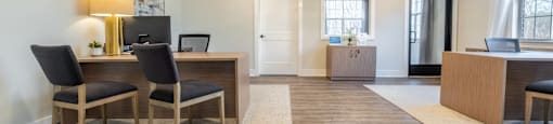 A room with a desk and chairs in the foreground and a doorway in the background in the clubhouse at Amelia Village apartments in Clayton, NC.