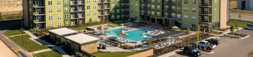 A large apartment complex with a pool in the middle of the parking lot at Boardwalk at Research Park apartments in Huntsville, AL.
