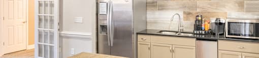 A kitchen with a wooden table and a refrigerator at 1322 North Apartments clubhouse in Auburn, AL.