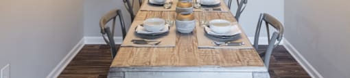 A dining room with a wooden table set for a meal at 1322 North Apartments in Auburn, AL.