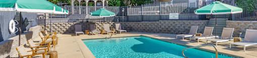 A swimming pool surrounded by chairs and umbrellas with 1322 North Apartments in the background in Auburn, AL.