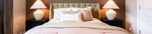 A Bed with a Pink Comforter, Throw Pills and Two Lamps on Nightstands.
