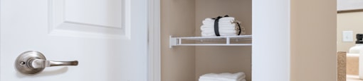A white door with a silver handle is open to a white shelf with towels on it.