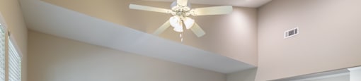 an empty living room with a ceiling fan and a kitchen