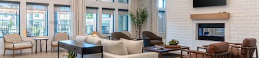 A clubhouse with a white couch, a black coffee table, and a fireplace with a flat screen TV above it at SW 38th Avenue Apartments in Ocala, FL.