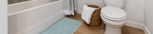 A bathroom with a toilet, a shower, and a basket on the floor.
