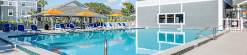 a large swimming pool with lounge chairs and umbrellas in front of a building