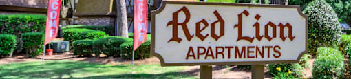 a red lion apartments sign in front of a yard with trees