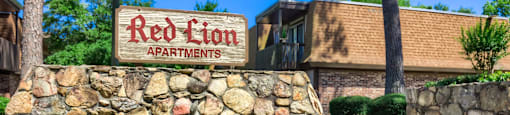 a pool with a fountain in front of the red lion apartments sign