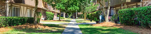 a sidewalk between two apartment buildings with green trees