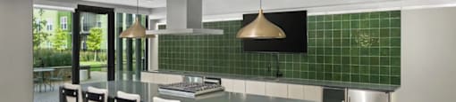 A kitchen with a green backsplash and a long island with chairs at Boardwalk at Research Park apartments in Huntsville, AL.