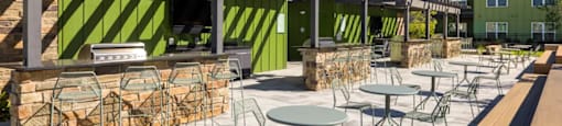 A patio with tables and chairs and a green building in the background at Boardwalk at Research Park apartments in Huntsville, AL.
