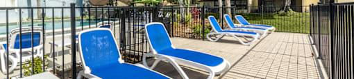 a patio with blue lounge chairs and a pool in the background