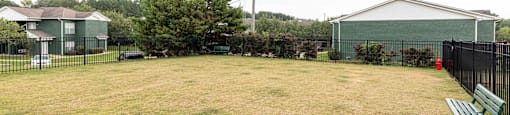A large grassy field with a bench and a fence.