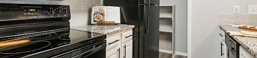 A black stove and refrigerator in a kitchen with white cabinets.