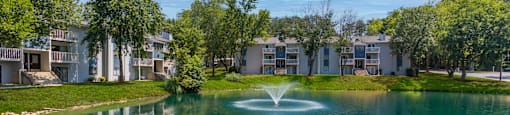 a fountain in the middle of a pond with apartments in the background