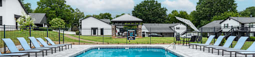 A swimming pool surrounded by lounge chairs and a fence.