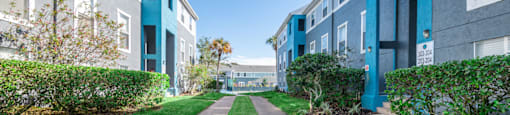 a walkway between two apartment buildings with green grass and bushes on either side
