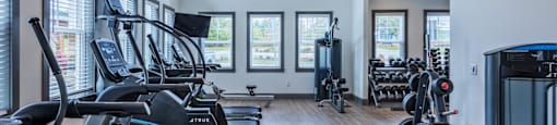 a gym with weights and cardio equipment in a building with windows