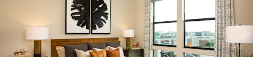 A bedroom with a large bed, a ceiling fan, and a view of the city at 27Seventy Lower Heights apartments in Houston, TX.