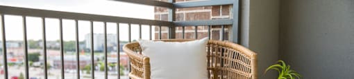 A wicker chair with a white cushion is placed on a balcony with a view of a parking lot at 27Seventy Lower Heights apartments in Houston, TX.