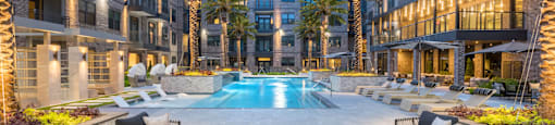 A fire pit near the pool in the middle of a courtyard surrounded by chairs and palm trees at 27Seventy Lower Heights apartments in Houston, TX.