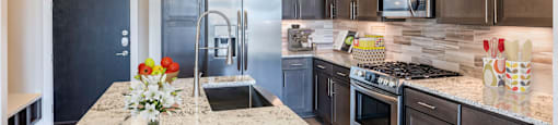 A kitchen with a granite countertop and dark brown cabinetsat 27Seventy Lower Heights apartments in Houston, TX.
