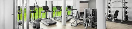 A gym with a variety of equipment including weights, a bench press, and a treadmill at Boardwalk at Research Park apartments in Huntsville, AL.