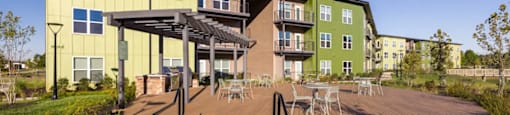 A wooden deck with a metal railing leads to a building with a green and yellow exterior at Boardwalk at Research Park apartments in Huntsville, AL.