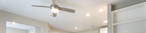an empty living room with a ceiling fan and shelves