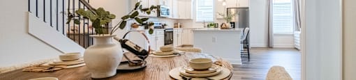 A dining table set with plates and bowls is in the foreground of a bright and modern kitchen.